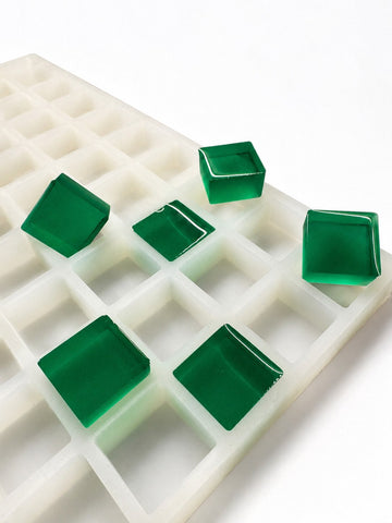 Side-angle view of a 6mL square gummy mold with 165 cavities and translucent emerald green square gummies on a white background